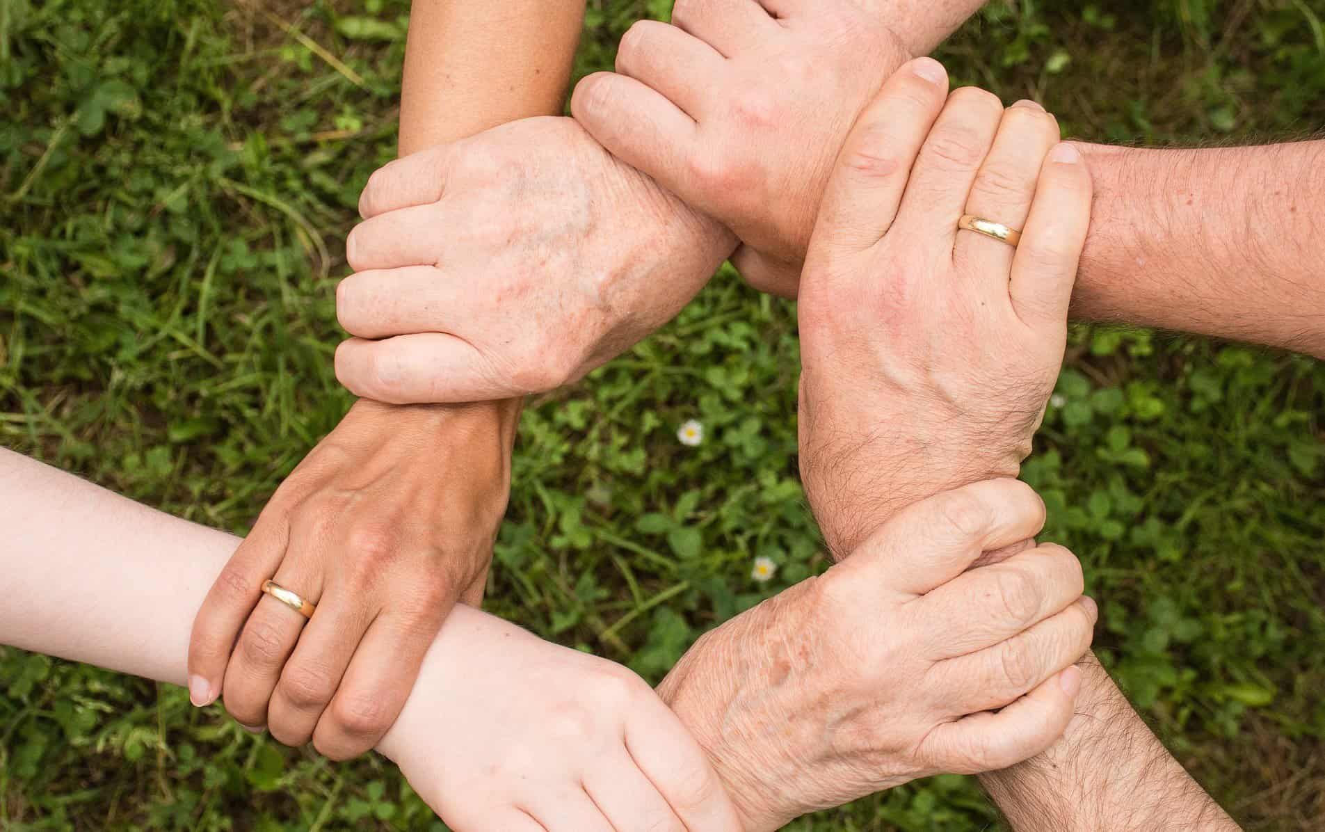 Six hands are shown over grass each holding another's wrists.