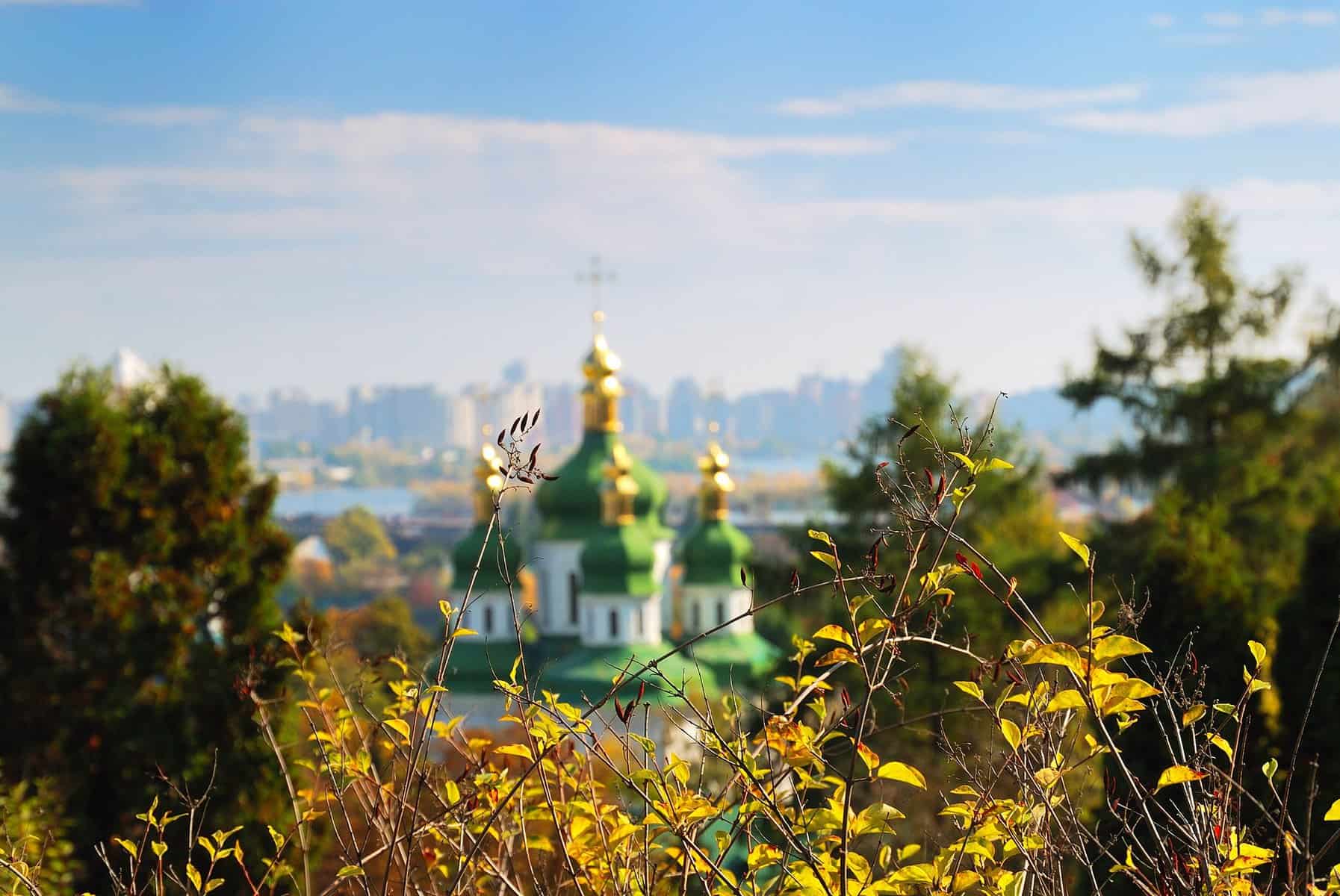 A blurred building in Ukraine is shown with its green domes topped with gold.