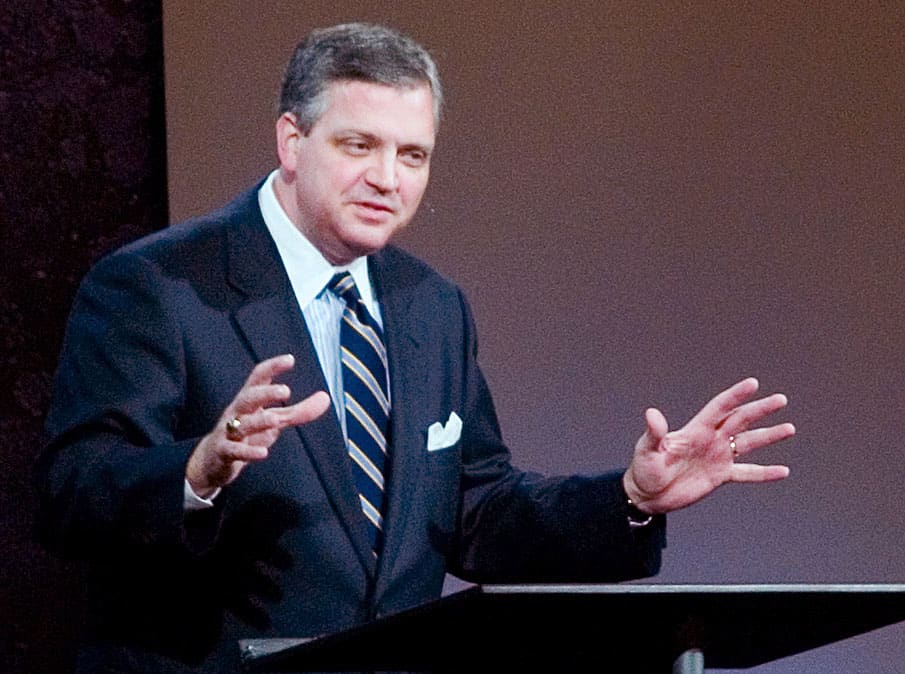 Al Mohler is shown speaking at a podium with hands raised.