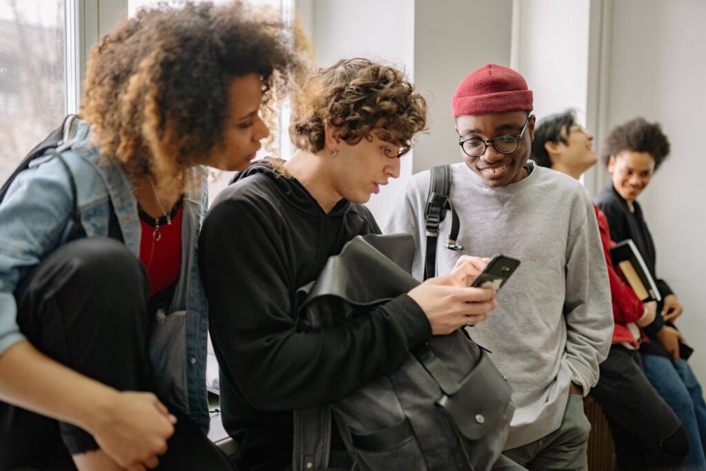 A diverse group of college students are shown looking at the phone of one.