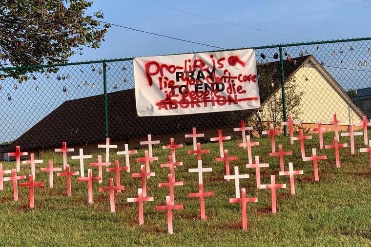A white banner hung over red and white crosses is defaced with red paint.