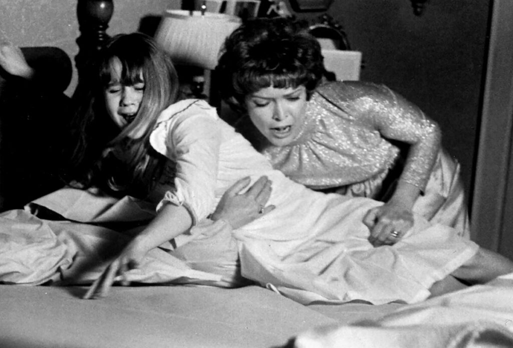A scene from The Exorcist with a woman trying to pick a young girl up off a bed.