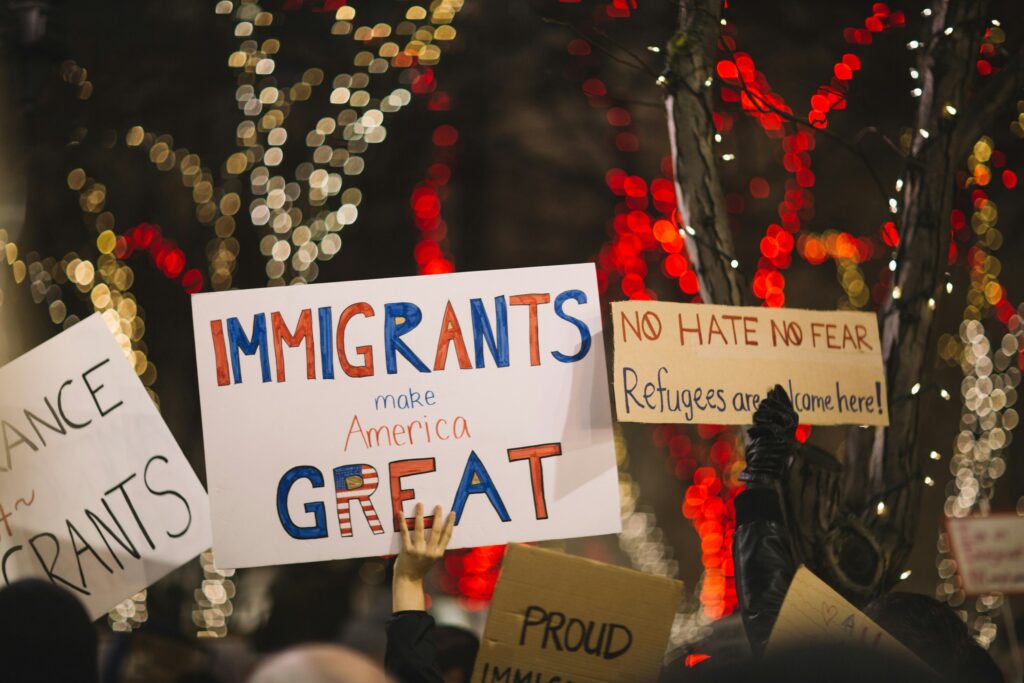 Pro immigrant signs are held up at night with colorful lights adoring trees behind them.
