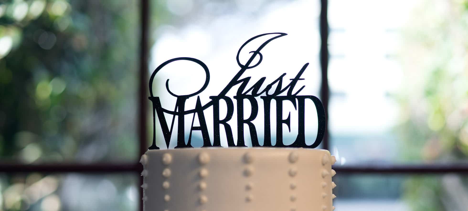A white wedding cake with a black metal topper that says "Just Married".