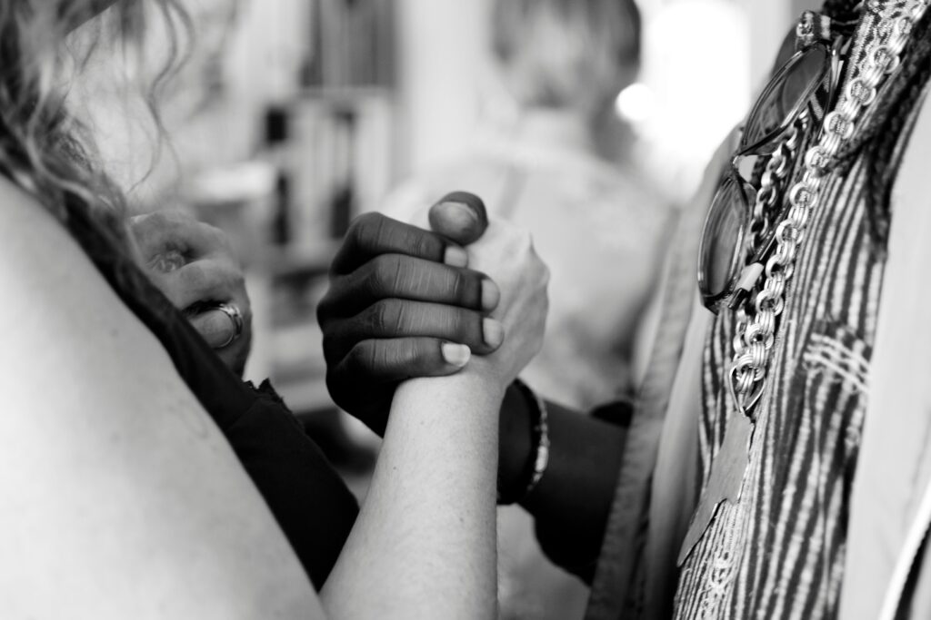 A white person and a Black person are shown facing each other and clasping hands at chest level.