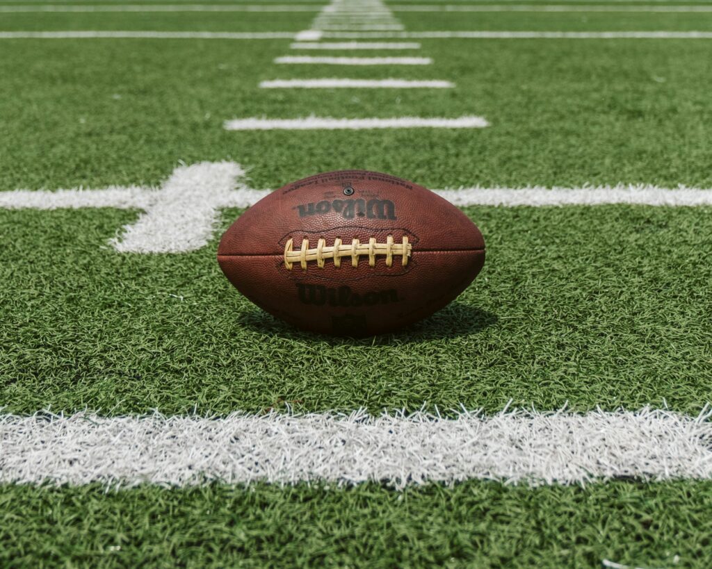An American football sits between marked lines on a green field.