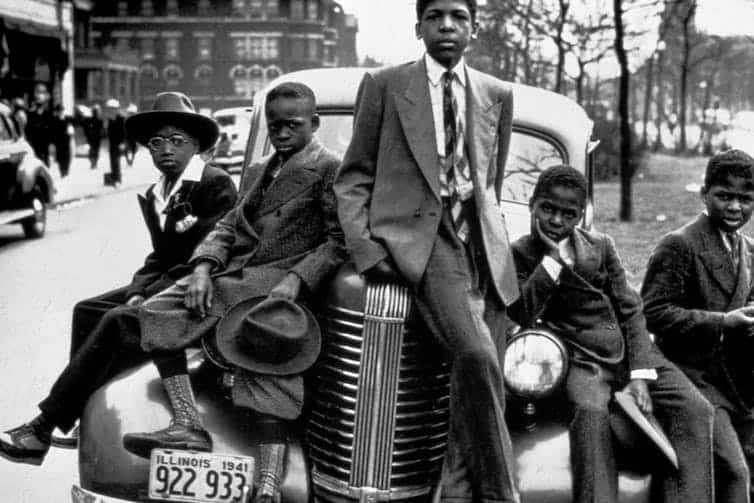 Five Black young men, dressed in suits, sit atop a white car with an Illinois number plate.