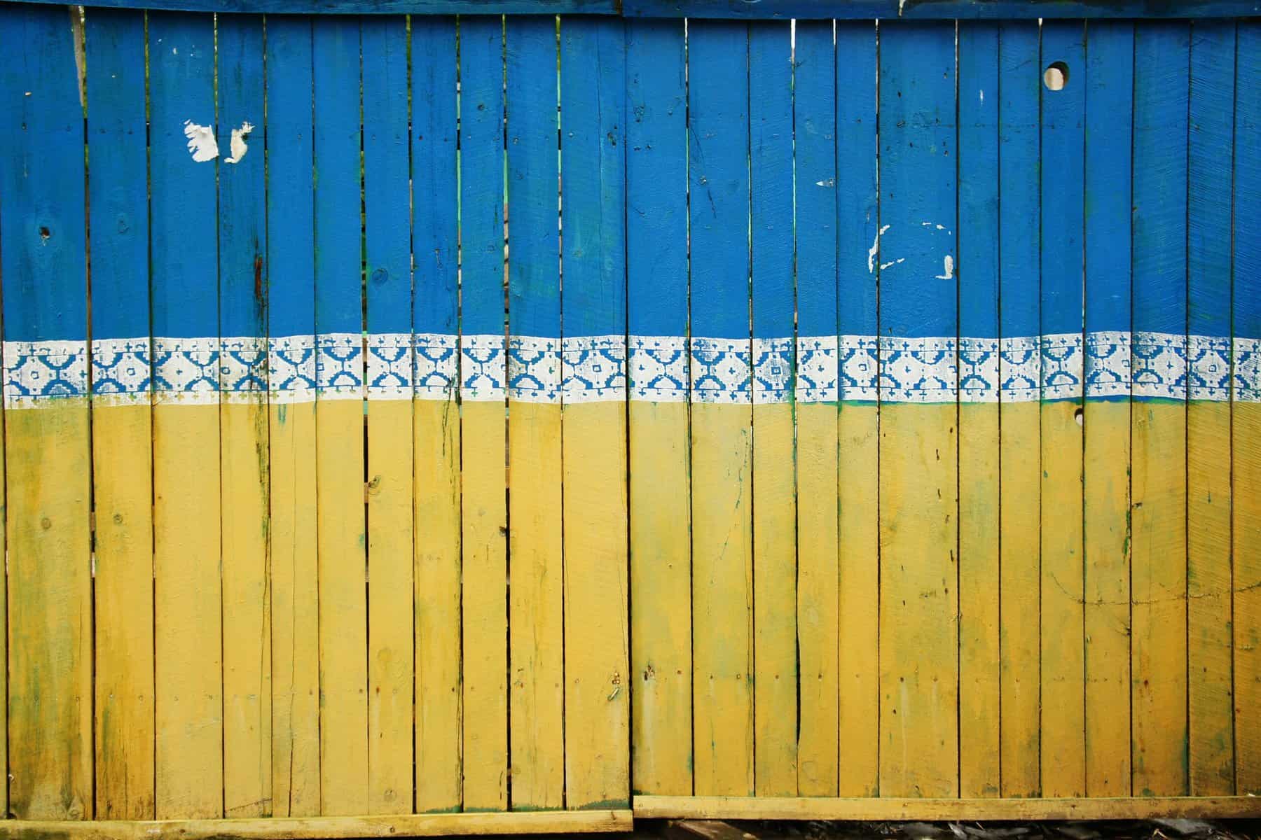 The colors of the Ukraine flag are painted across wooden fence boards.