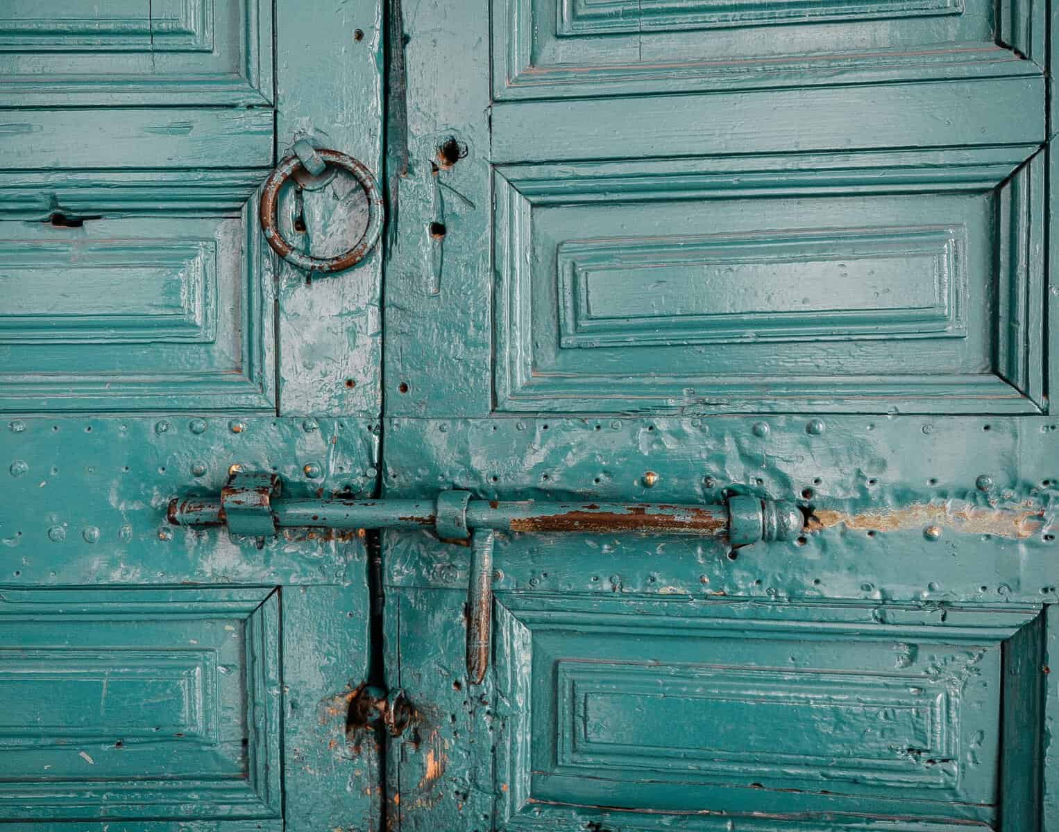 A set of old soft teal doors are shown close up with a slide lock.
