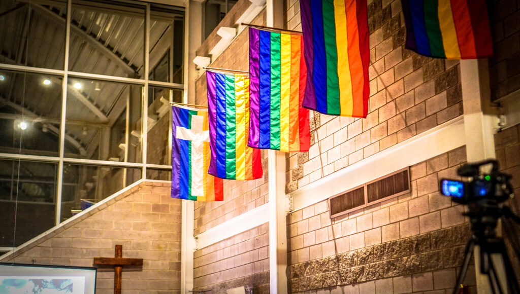 Pride flags hang on an interior stone wall.