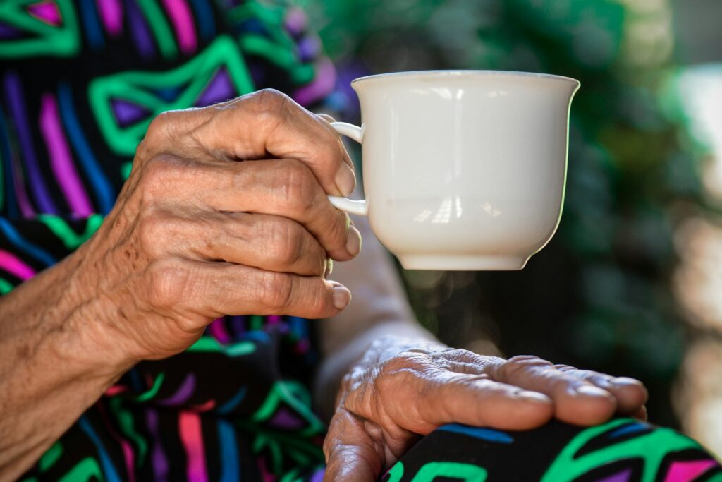 Nursing homes struggle as foreign-born caregivers exit under new rules An elderly woman's hand holds a coffee cup.
