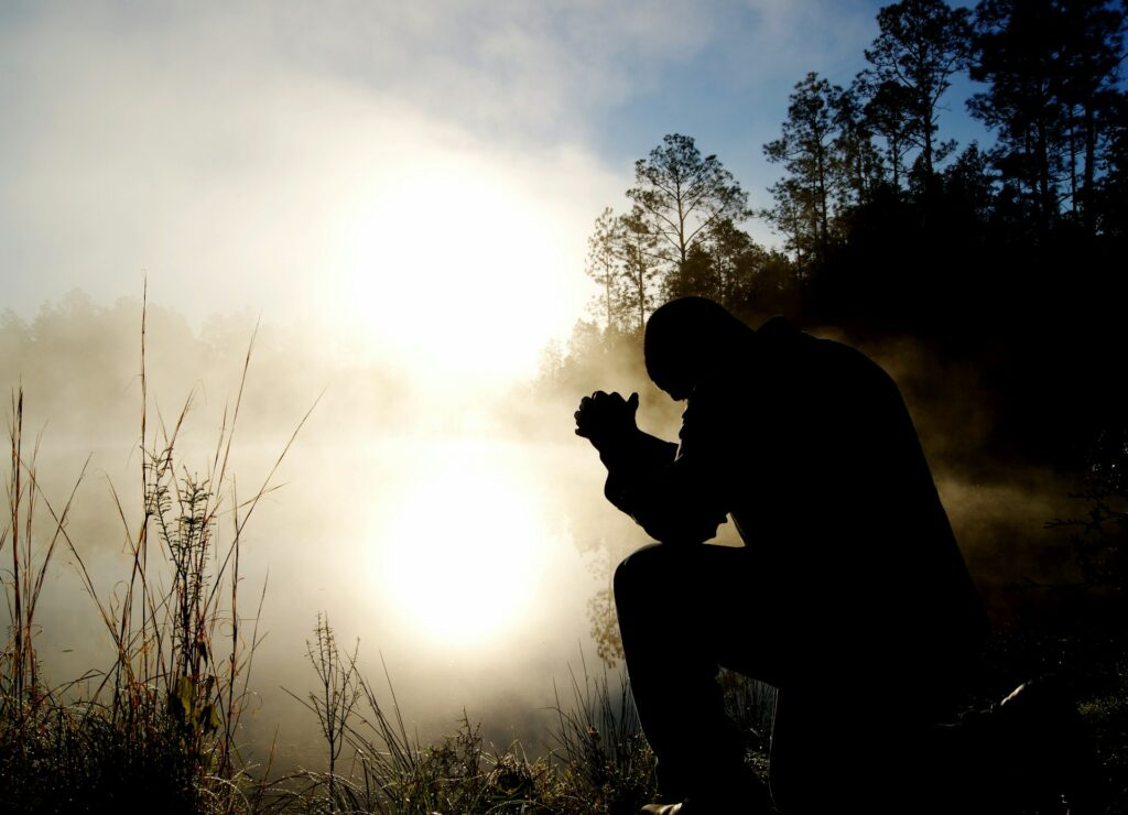 A man sits with clasped hands and bowed head.