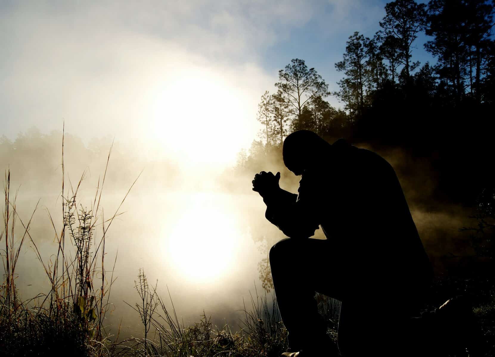 A man sits with clasped hands and bowed head.
