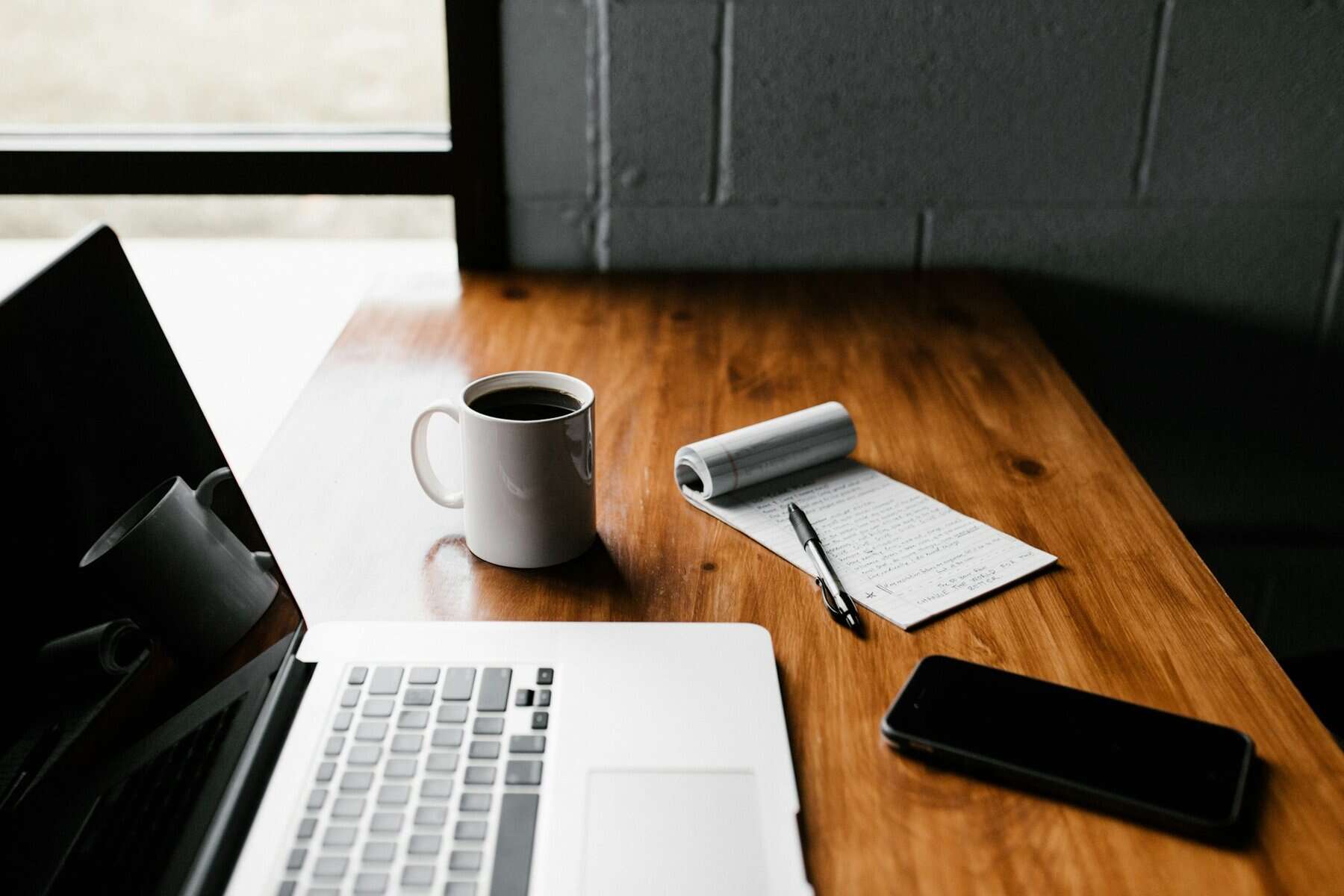 A desk with a laptop , notepad and cup of coffee.