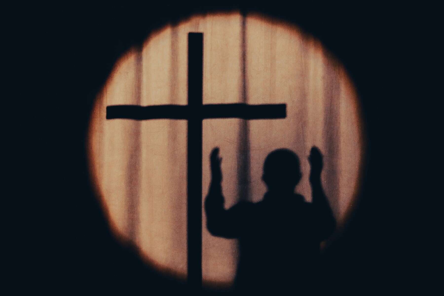 Shadow of a cross and a person with arms raised.