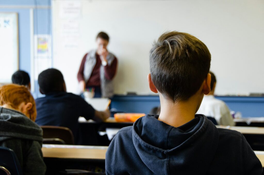 A boy sists in a classroom with his back to the camera.