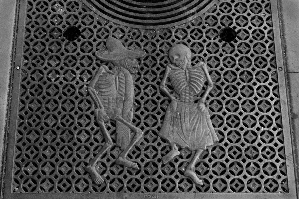 When the Darkness Comes (Psalm 23:4) Two skeletons dancing on an iron street grate in San Francisco's Mission District.