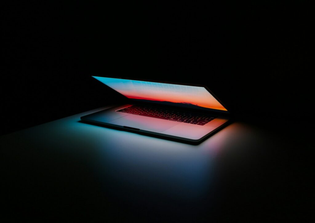 A laptop in a dark room slightly open with a colorful screen.