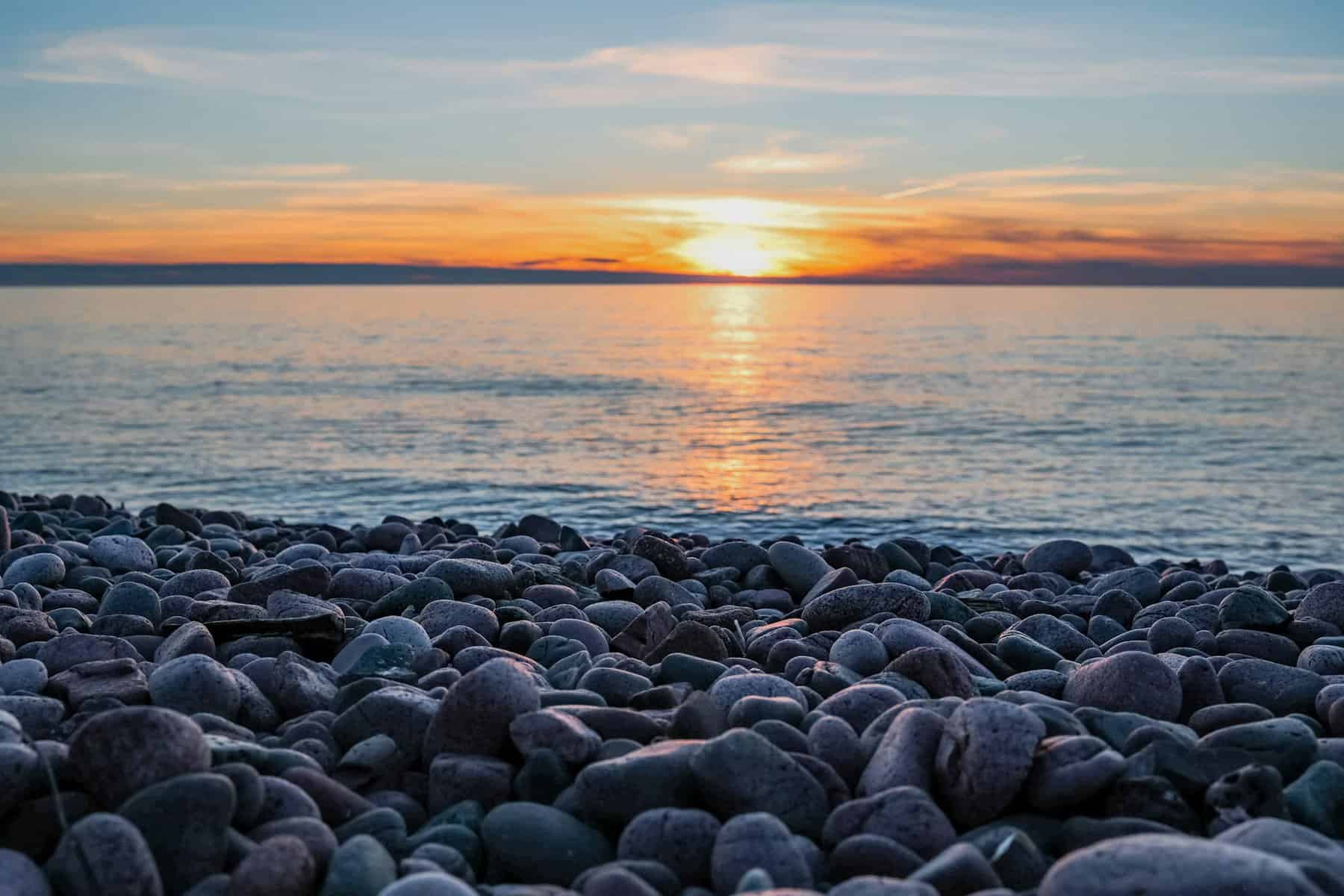 Sunset over Lake Superior with the rocky shore in the foreground.