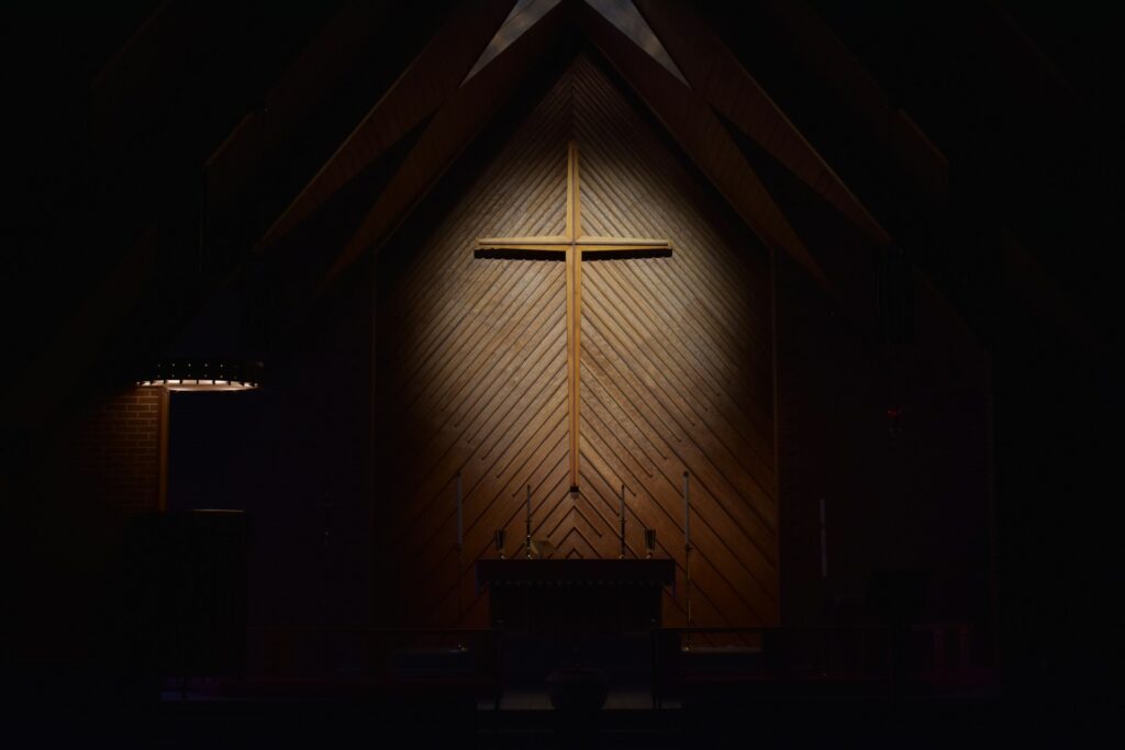 A dimly lit wooden cross hanging on a wooden wall.
