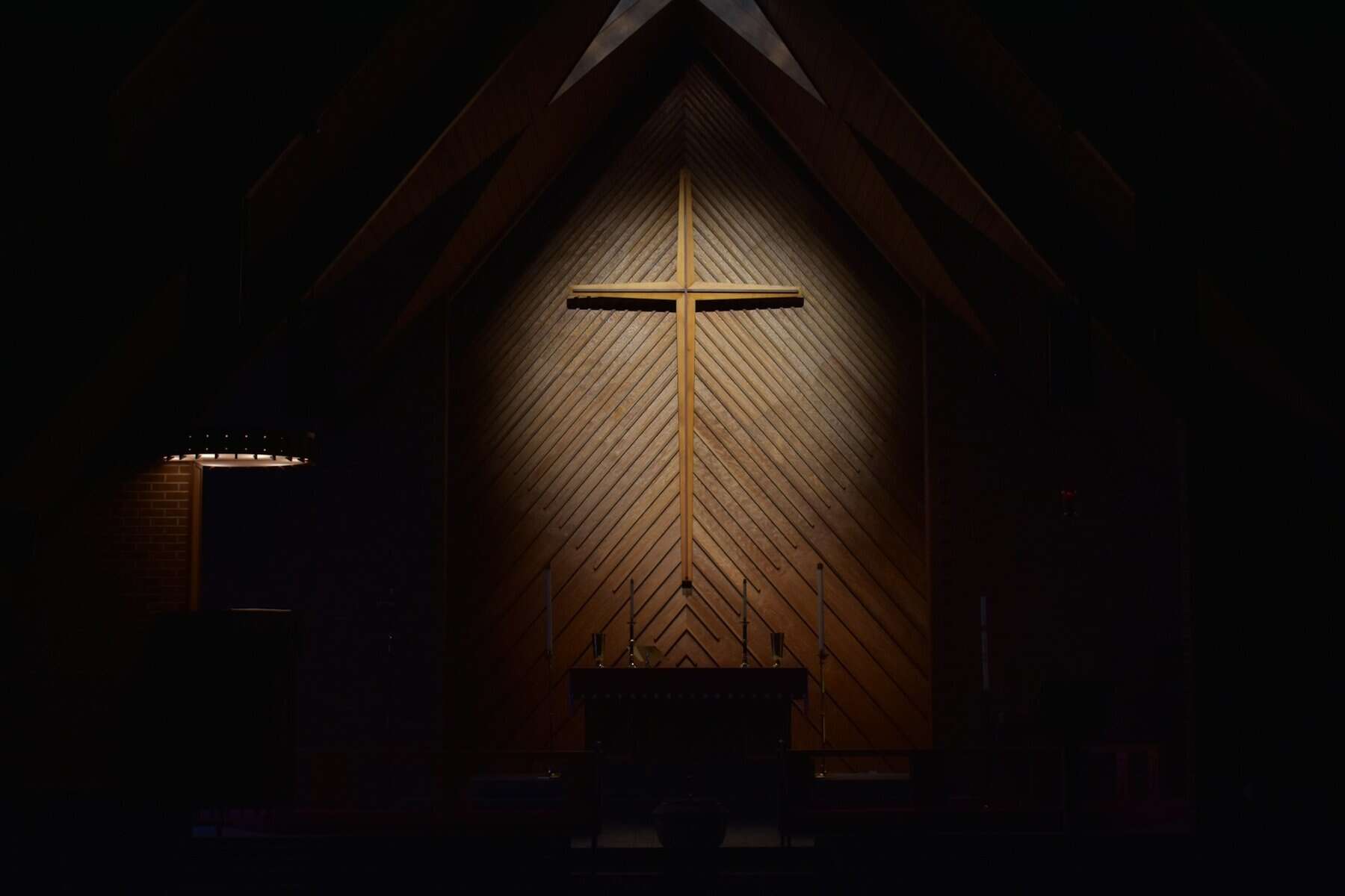 A dimly lit wooden cross hanging on a wooden wall.