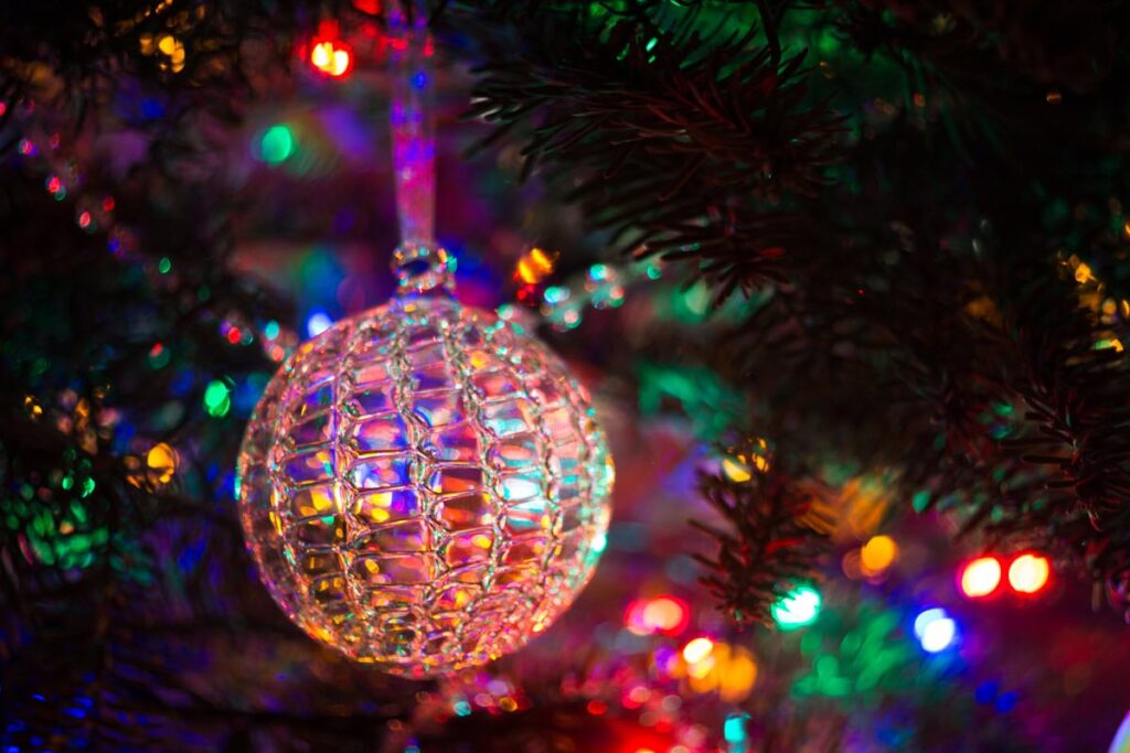 A spun glass Christmas ornament hanging on a Christmas tree lit with colored lights.