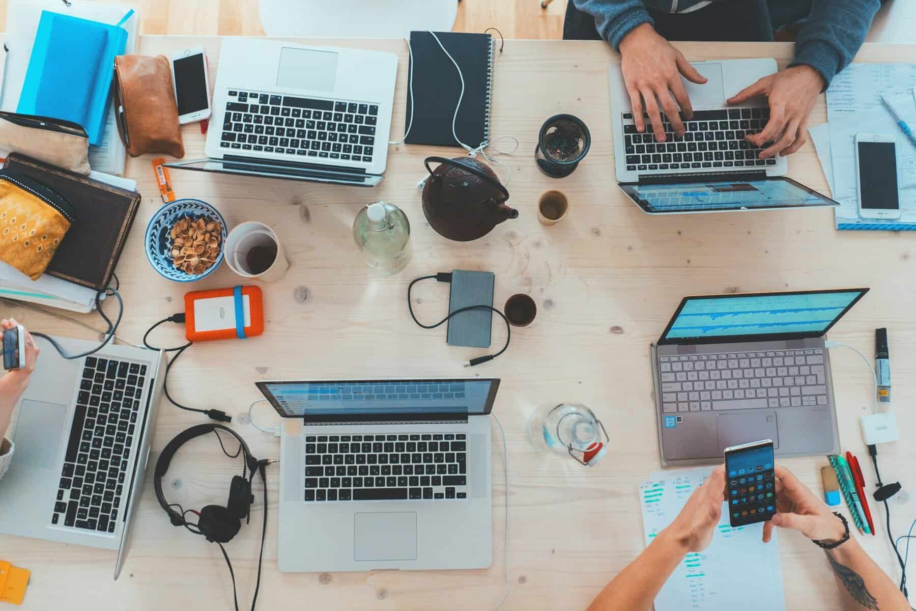 Laptops on a table surrounded by coffee cups and people.