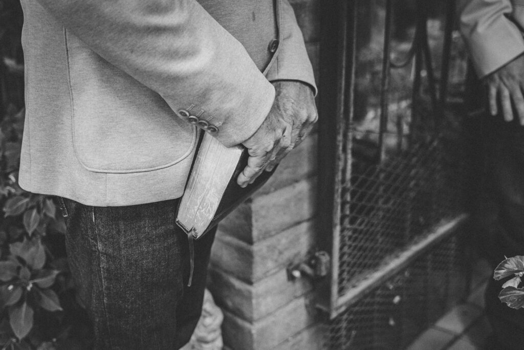 Black and White close-up image of a man holding a Bible down in front of himself.