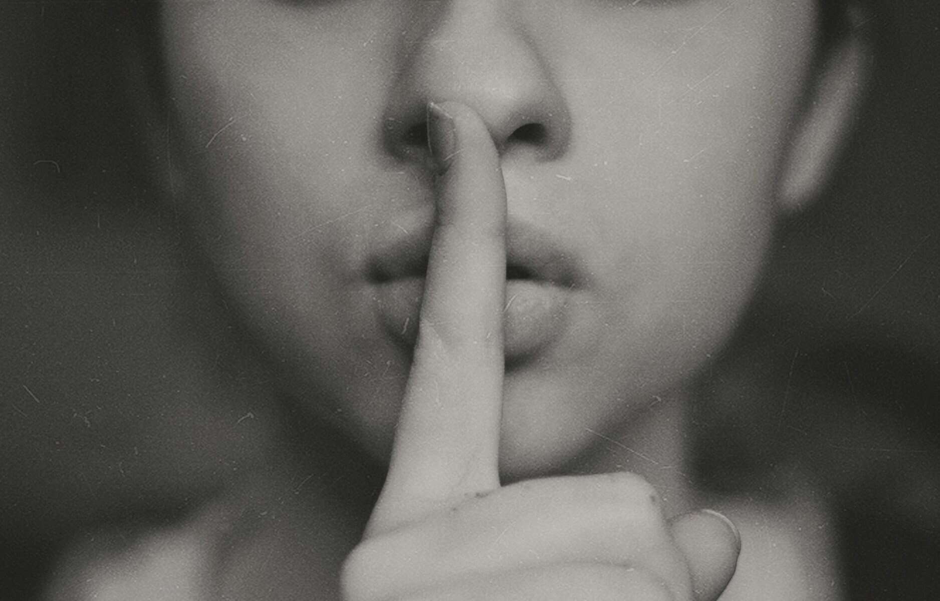 A woman with her index finger at her lips.