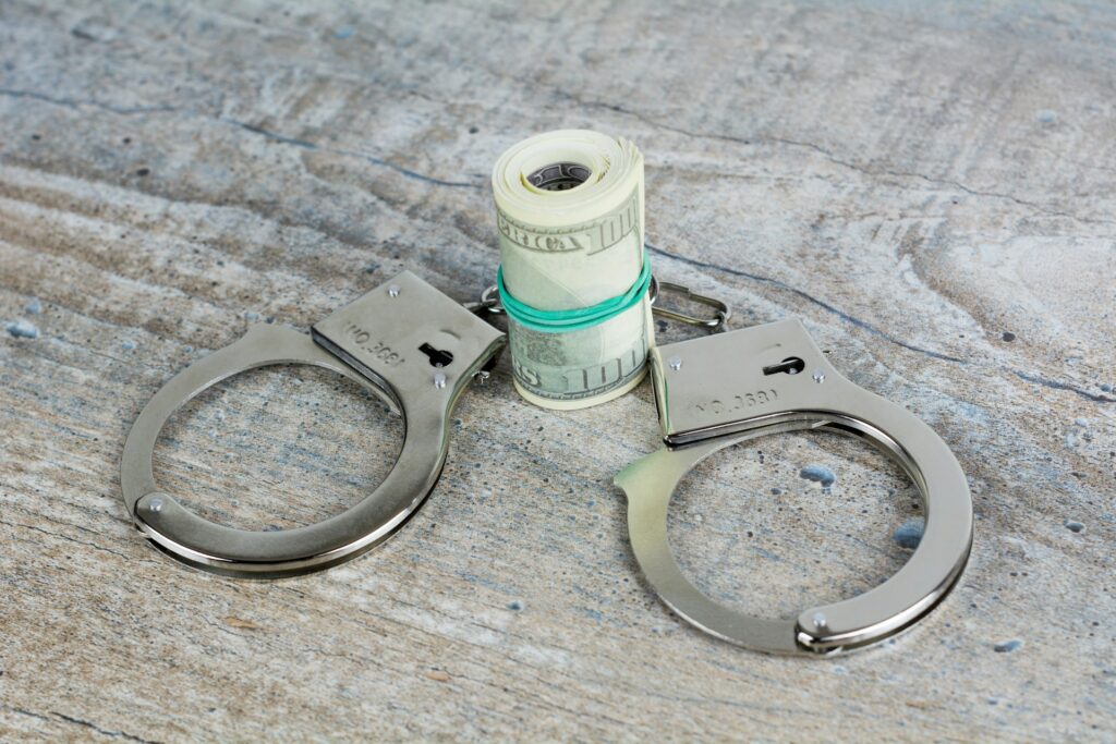 Handcuffs are shown with a large roll of U.S. 100 dollar bills.