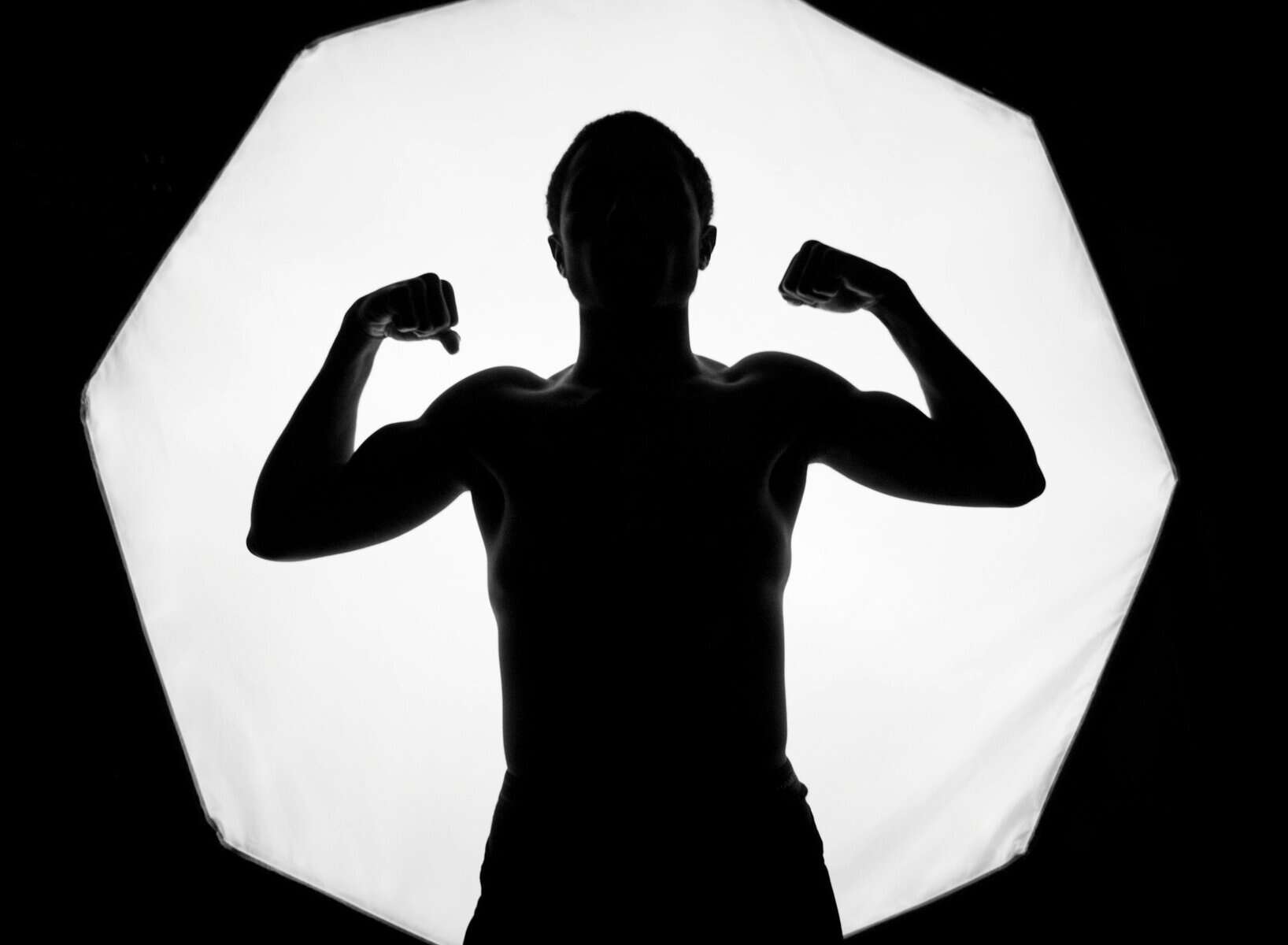A man in silhouette flexes his muscles.