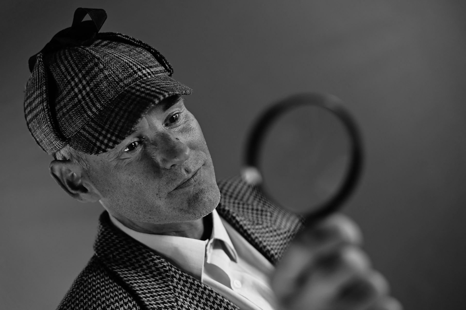 A man dressed like Sherlock Holmes holds a magnifying glass.