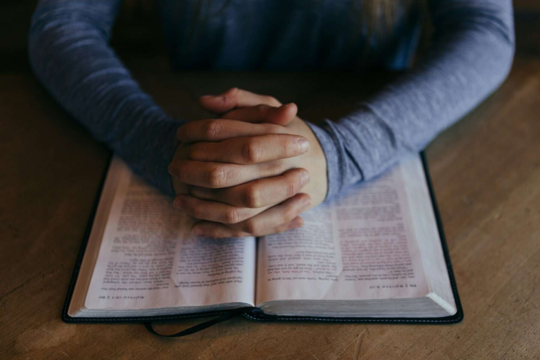 Folded hands resting on an open Bible.