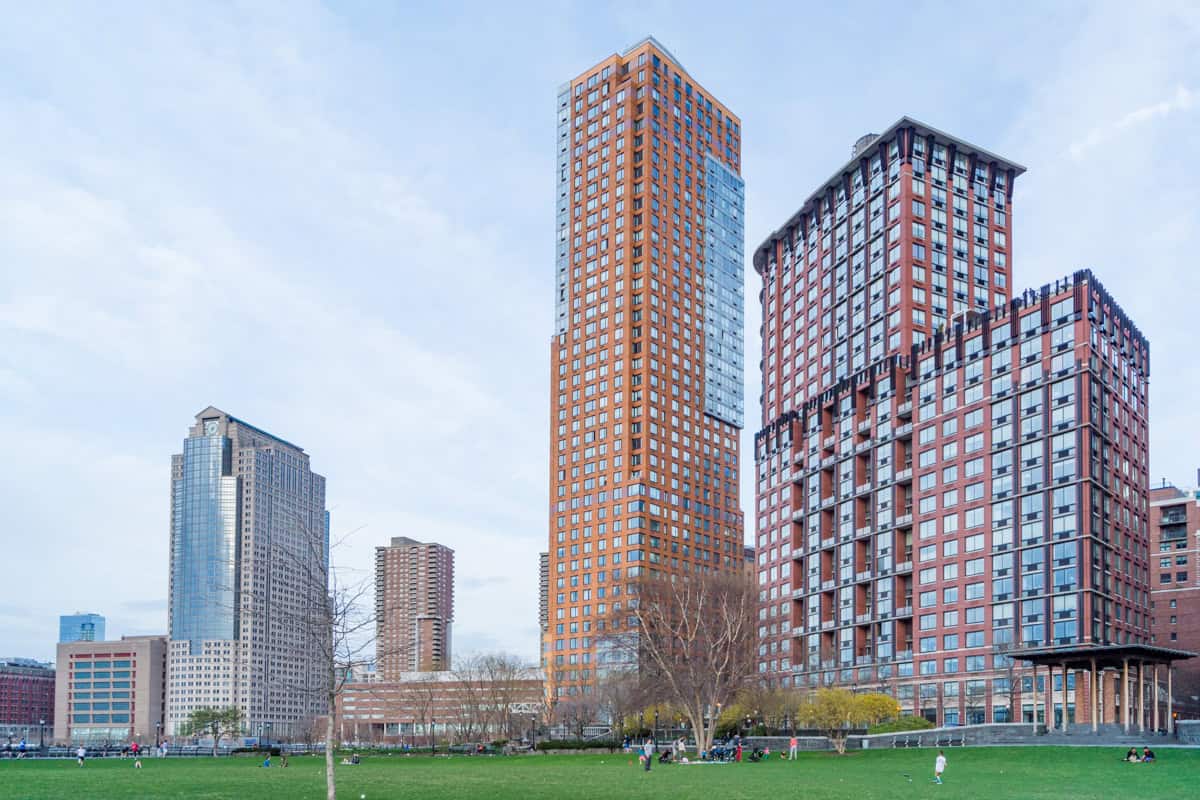 A view of Hudson River Park in New York City with skyscrapers as the backdrop to a green park in which people relaxing.