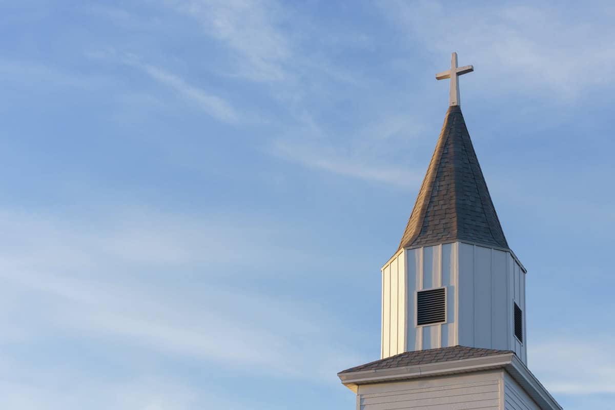 An old wooden church steeple against a blue sky with wispy clouds.