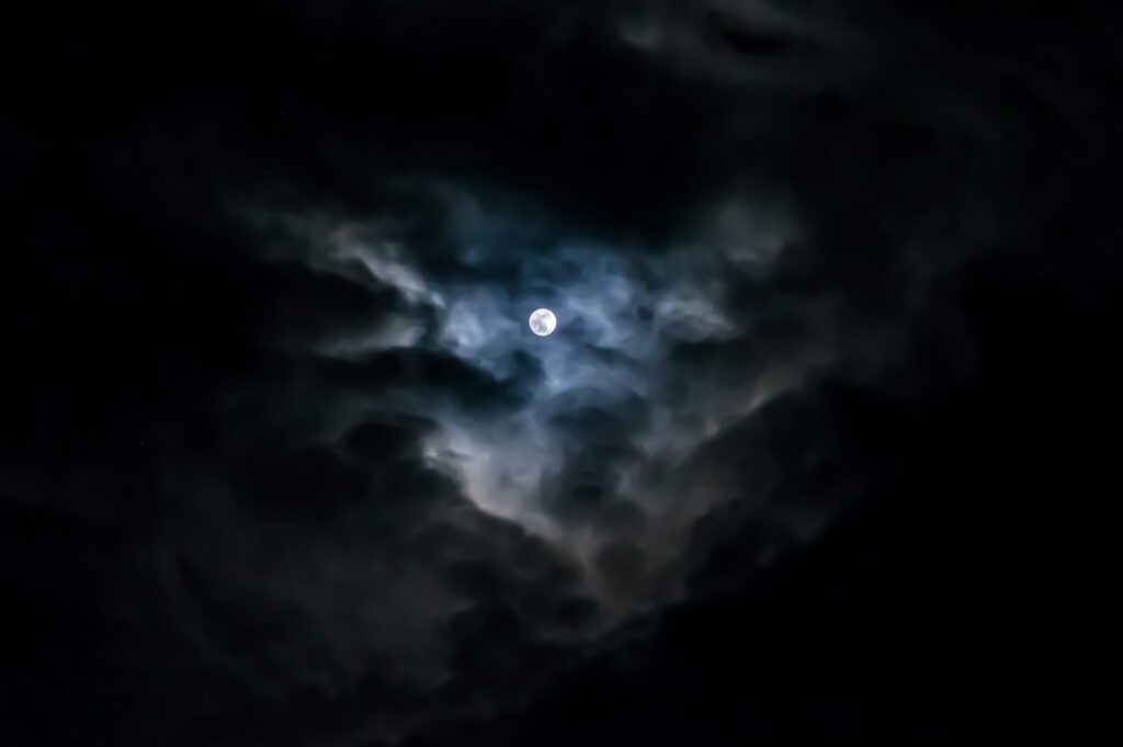 The moon seen through dark, ominous clouds.
