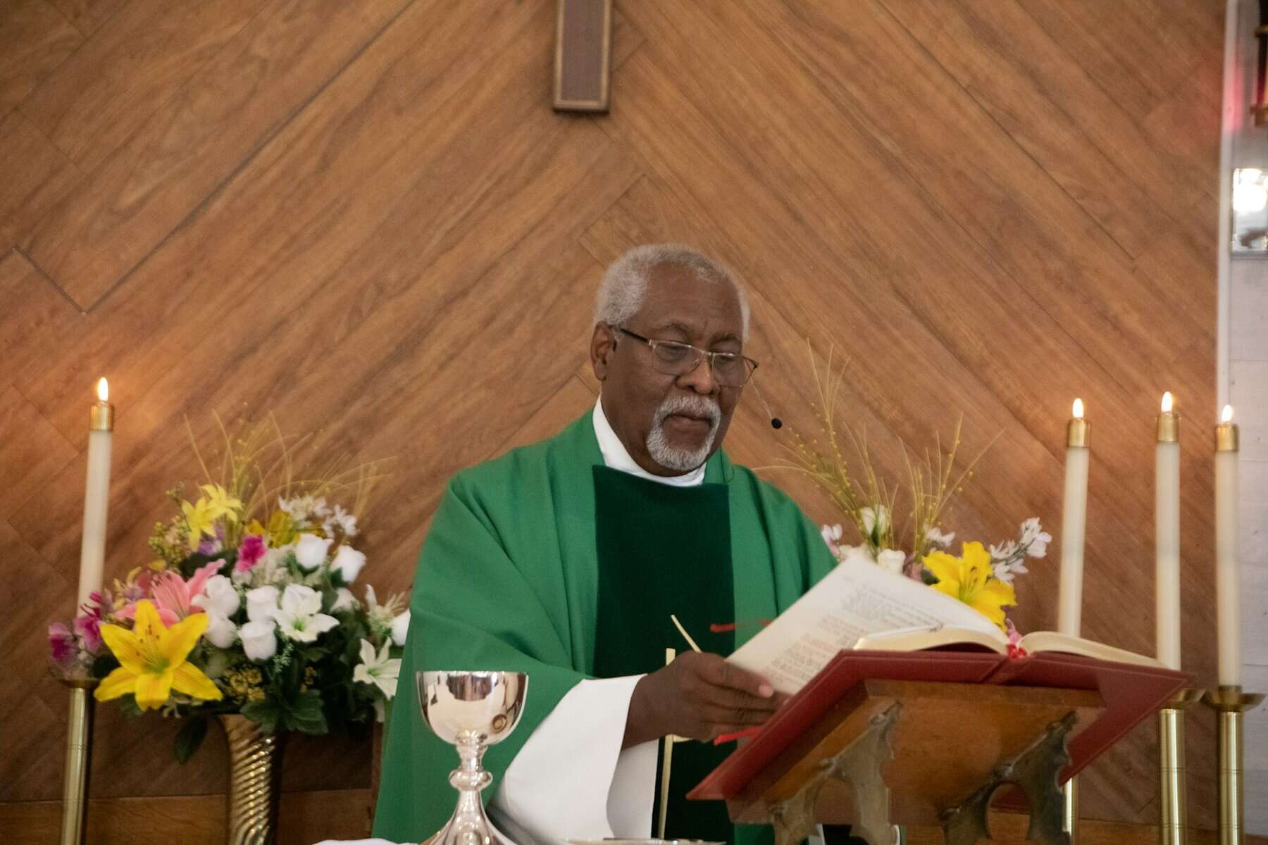 A Black male priest stands at an altar with a Bible.