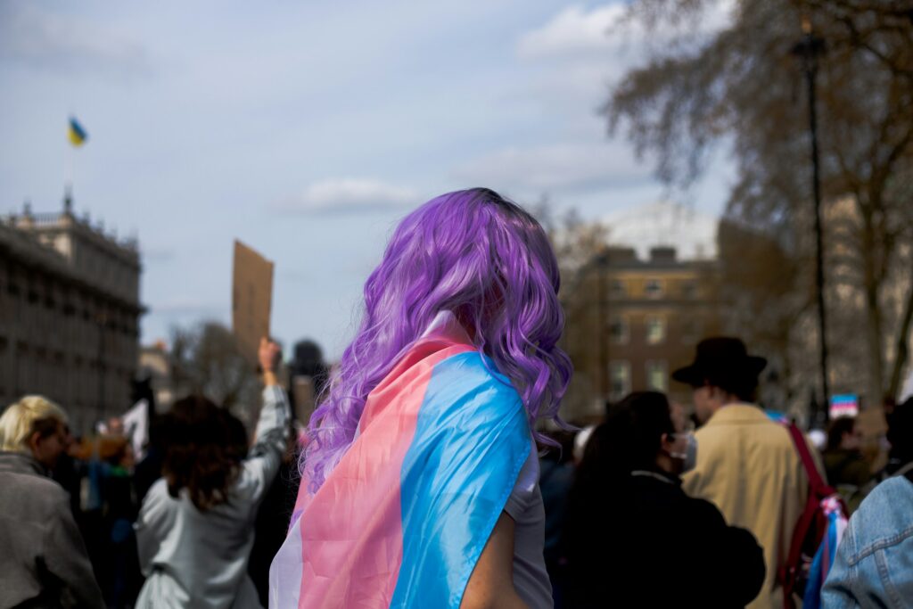A person in a crowd with a Trans flag wrapped around them.