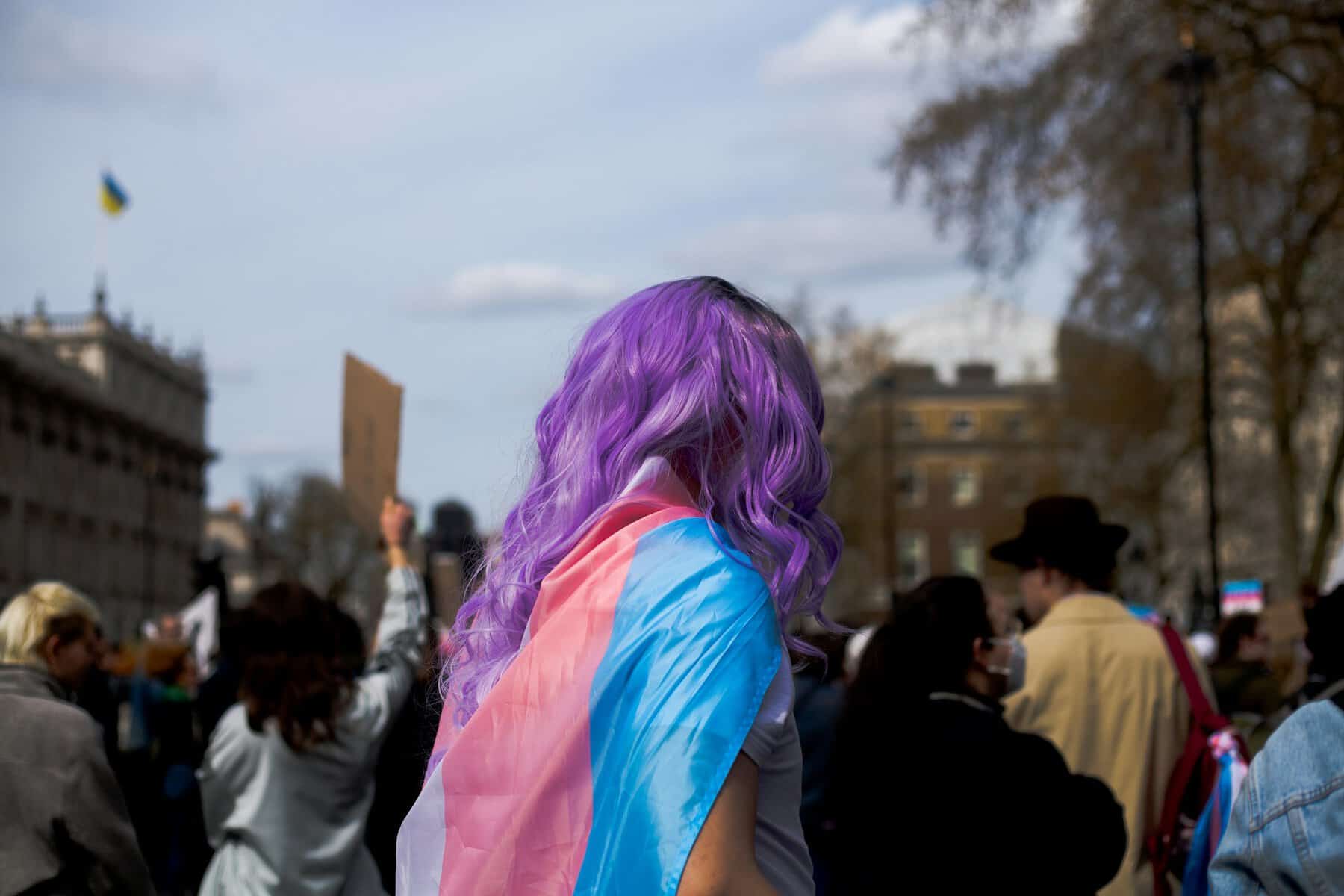 A person in a crowd with a Trans flag wrapped around them.