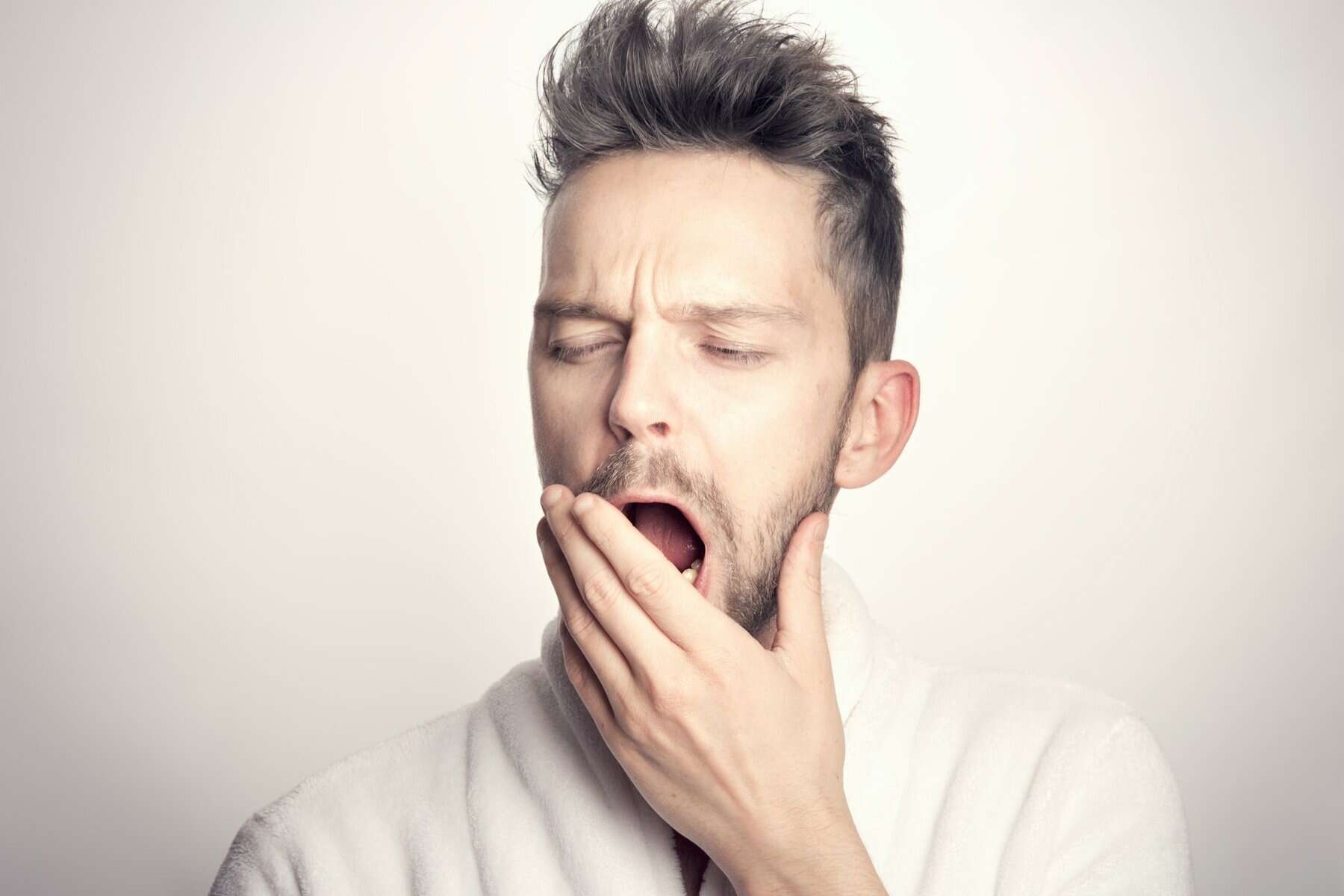 A White man with a short haircut yawning with his hand partially over his mouth.