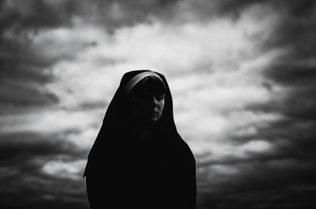 Black and White image of a woman in a nun's habit against a moody sky.