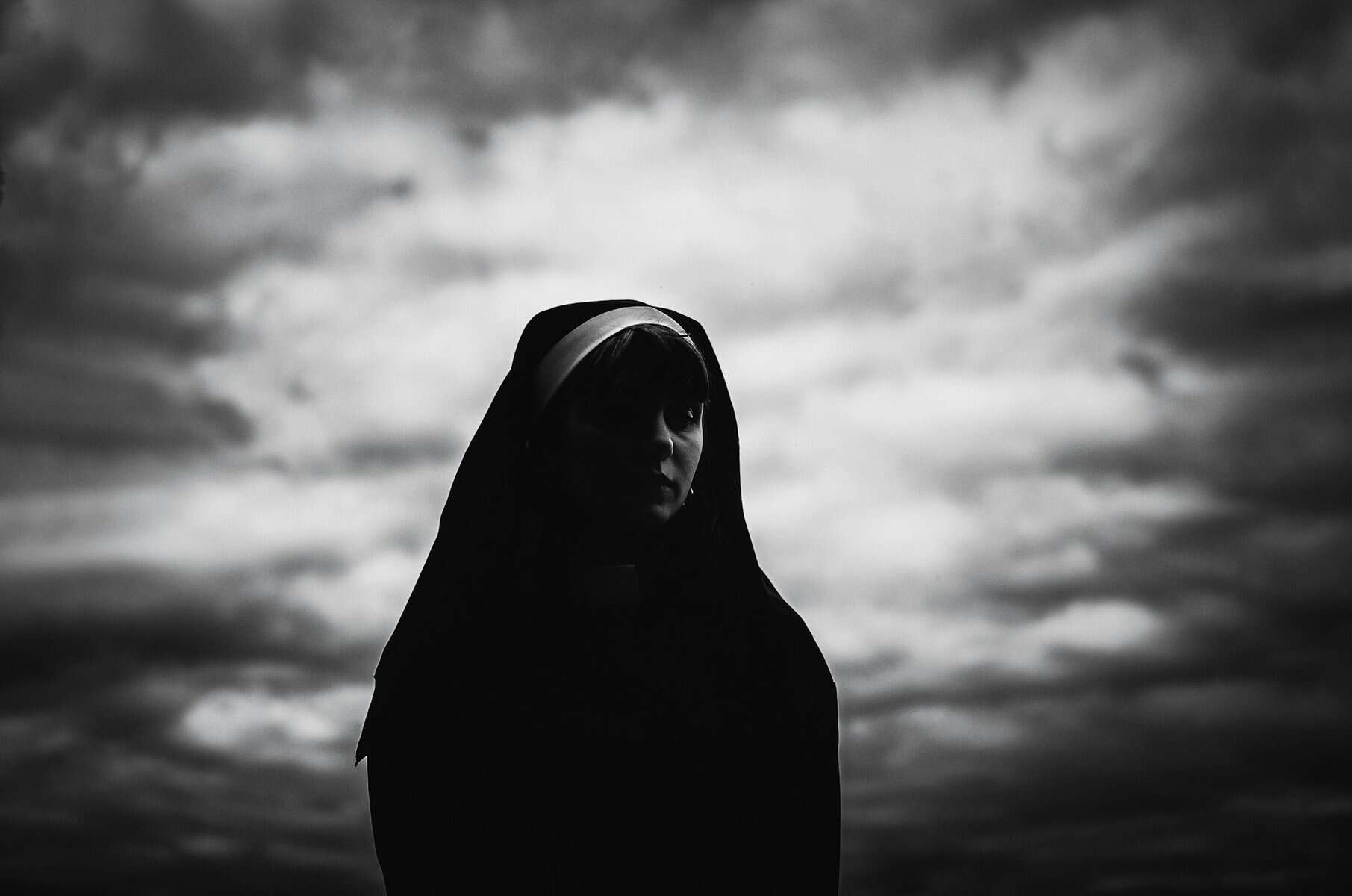 Black and White image of a woman in a nun's habit against a moody sky.