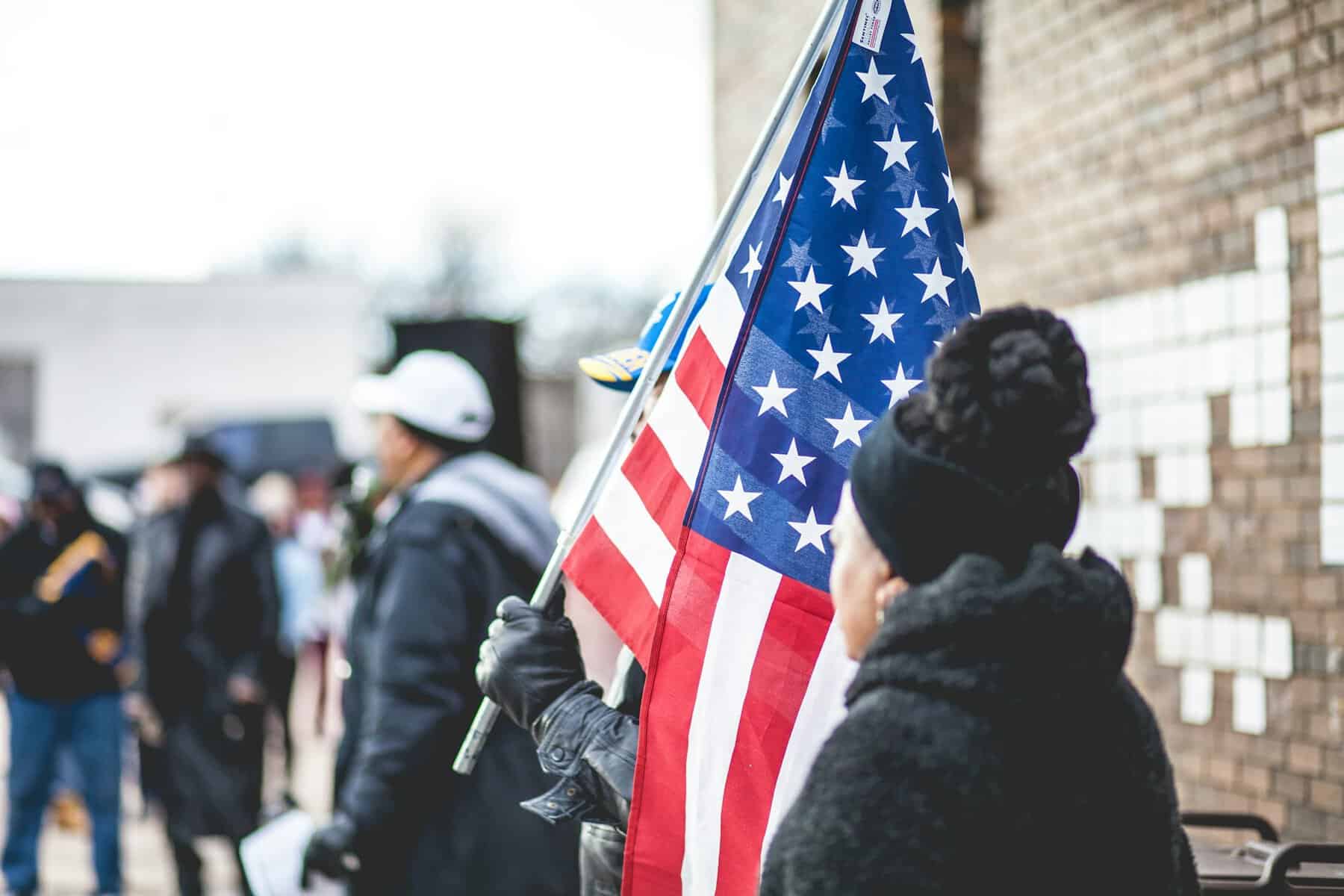 A person holding a large US flag in a crowd.