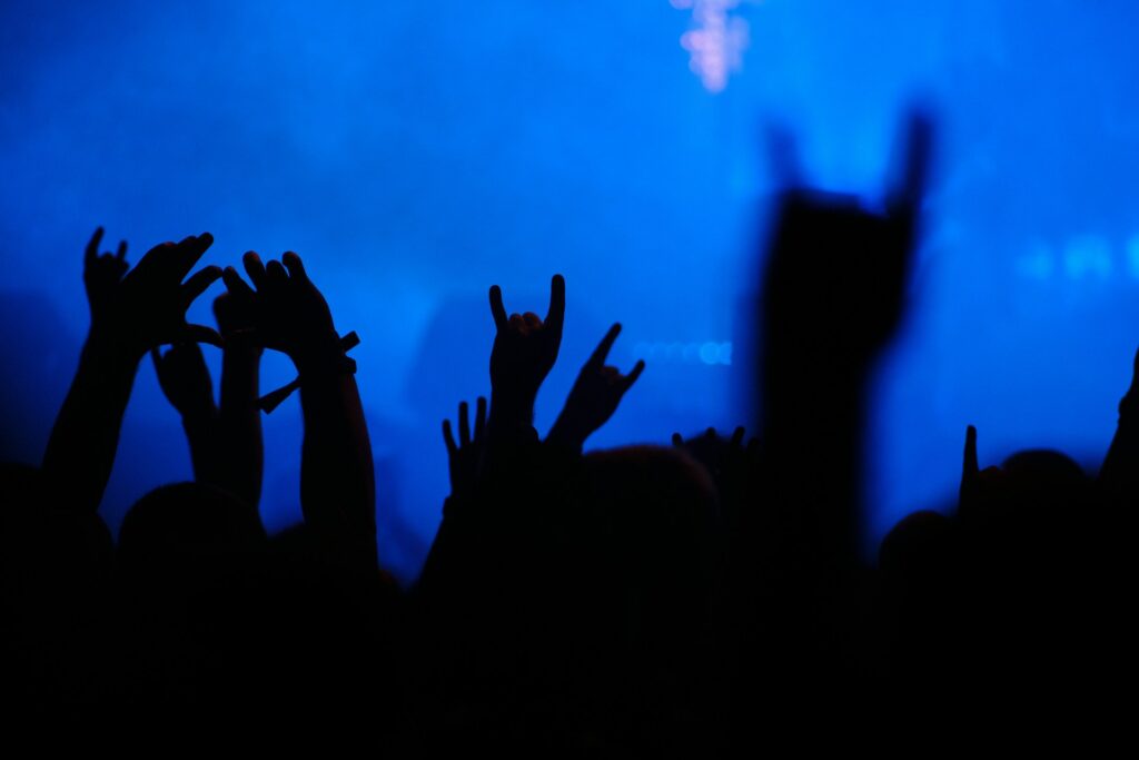 People raising their hands symbolically at a concert in low, blue light.