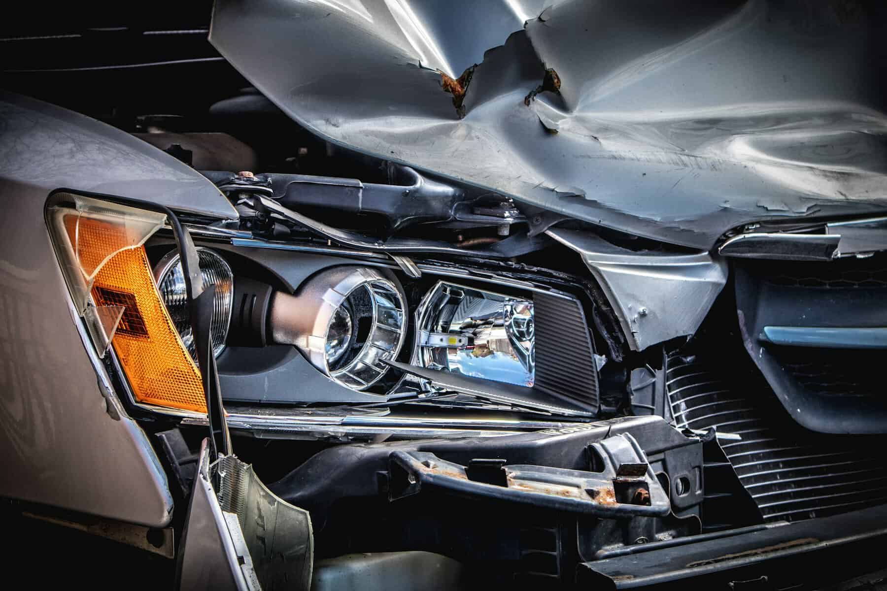The front side of a grey car that has been severely dented.