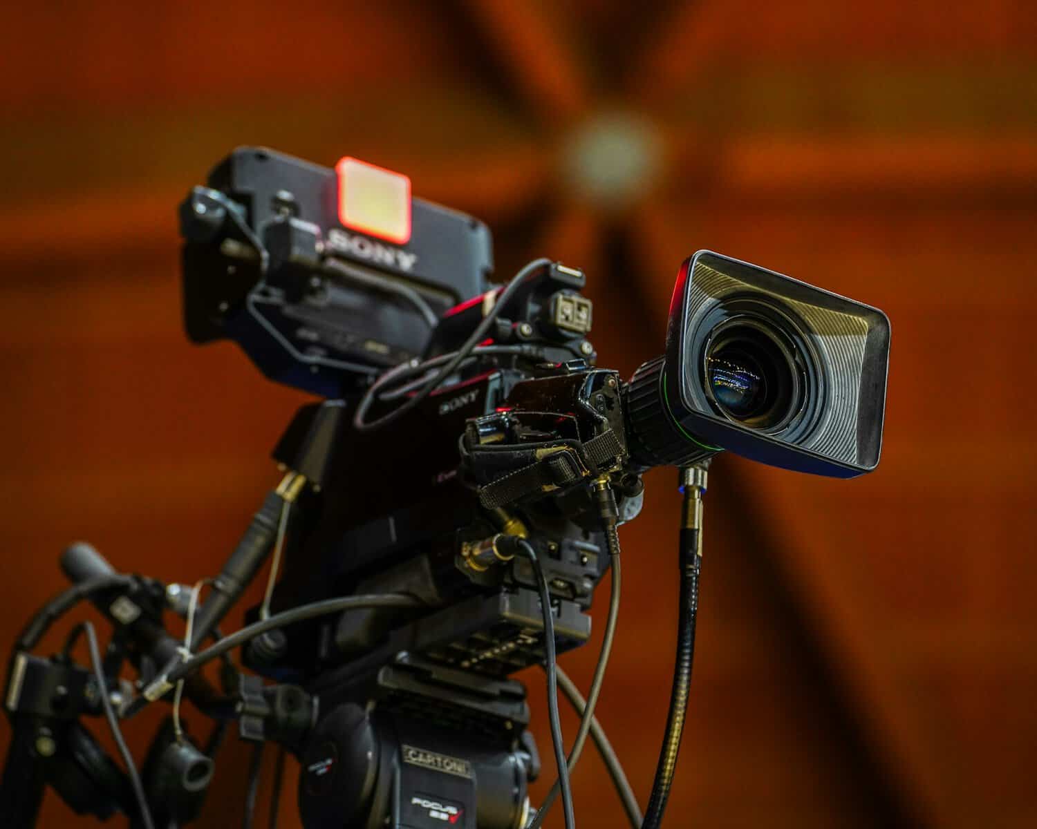A professional TV camera with a wooden church-like ceiling above it.