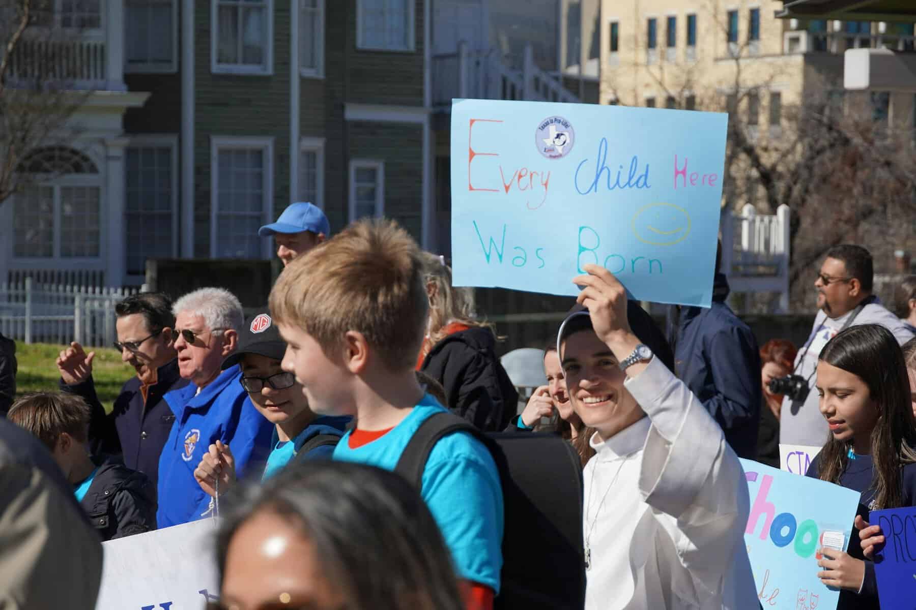A protester holds up a sign saying "every child here was born."