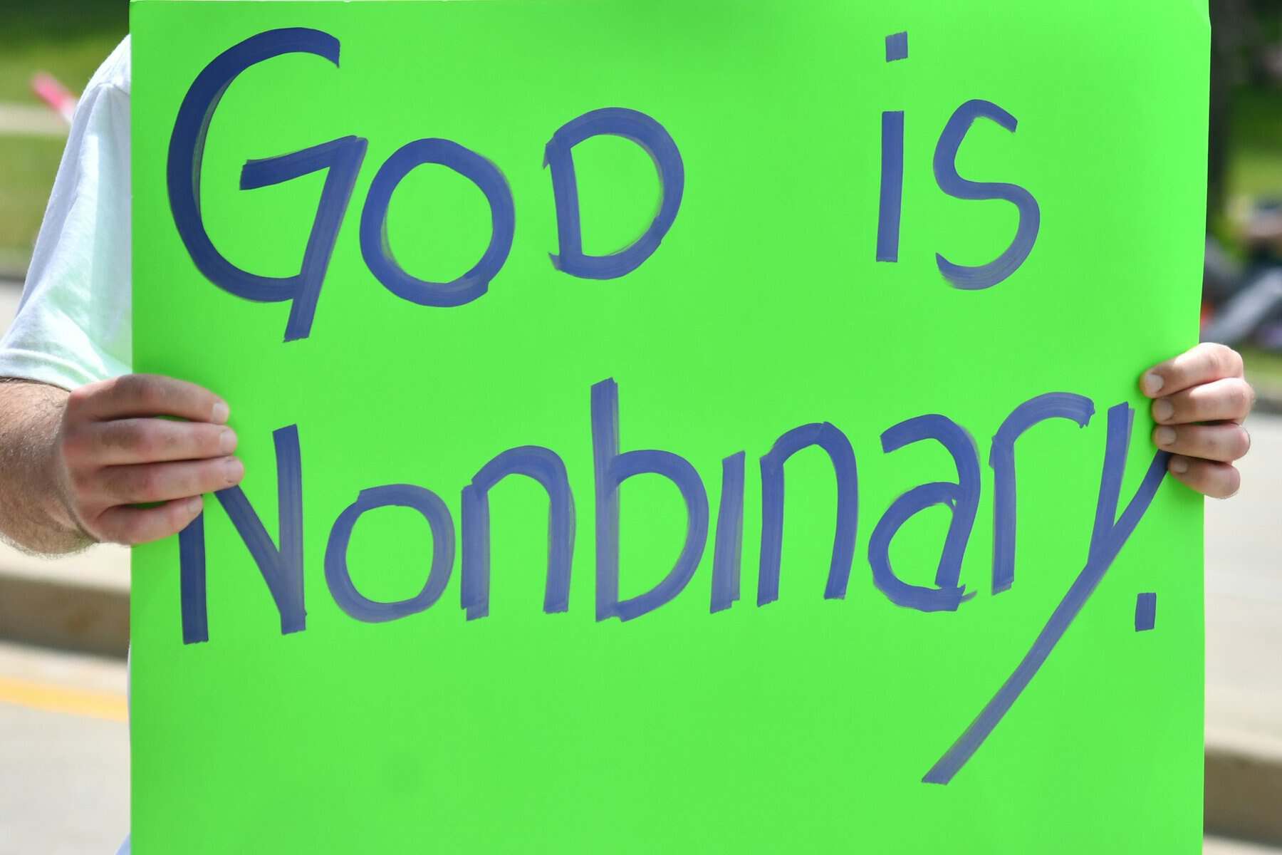 A neon green protest sign stating that God is nonbinary.