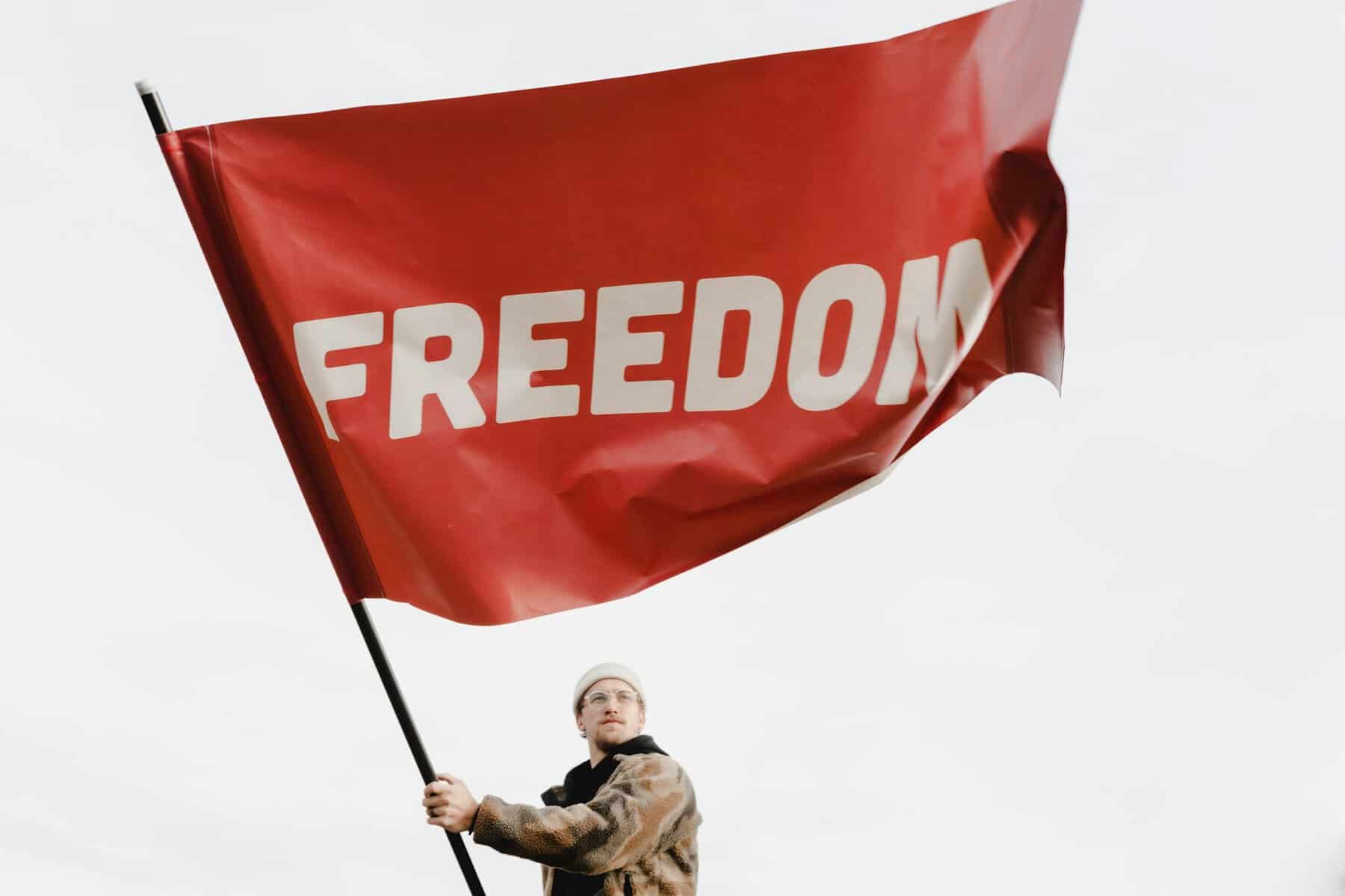 A man dressed in winter gear holds a large red flag that says Freedom.