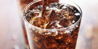 Image shows a glass of ice with brown soda being toped off.
